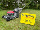 A Honda walk-behind lawn mower with a red engine cover is parked on grass next to a bright yellow sign that reads 'MARTINS OUTDOOR POWER' with a phone number and location.