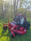 A red Ferris lawn mower with a large engine and rear tire, photographed outdoors on green grass with trees in the background.