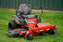 A red and gray zero-till riding lawn mower with 'BIG DOG' and 'ALPHA MP' branding, parked on a green grass lawn in front of a dark green fence.