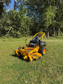 yellow and black zeroturn mower on a lawn with trees in the background
