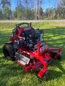 A red and black Fearis commercial lawn mower with a large engine, parked on a green grassy field with trees in the background.